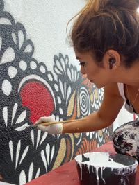 Gita Kurdpoor painting the mural with a brush, working on the wall.