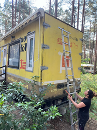 Artist holding a brush and adjusting a ladder in front of the tiny house