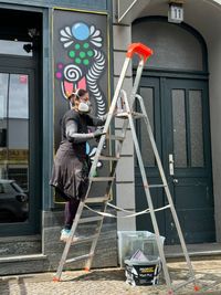 Artist Gita Kurdpoor on a ladder working on the caf&eacute; facade